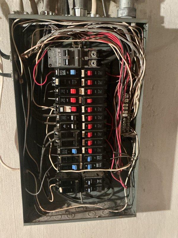 # Electrical Service - Whole Home Inspection

Performed comprehensive electrical inspection of 2-story freestanding condominium for recently purchased property. Conducted thorough evaluation of main electrical distribution panel, circuit breaker configuration, and overall system integrity.

## Primary Findings and Actions

Inspected main electrical panel box and documented existing conditions. Panel contains multiple circuit breakers with mixed configuration including standard black breakers, red switches, and blue toggle breakers. Identified two larger main disconnect switches or primary breakers at top of panel in gray/silver finish. Verified grounding bus bar connections on right side of panel with multiple wire terminations present.

Evaluated wiring organization and routing throughout panel interior. Observed numerous conductors including black, white, red, pink, beige/tan, and yellow insulated wires of various gauges entering and exiting panel box. Wiring extends from top of pane