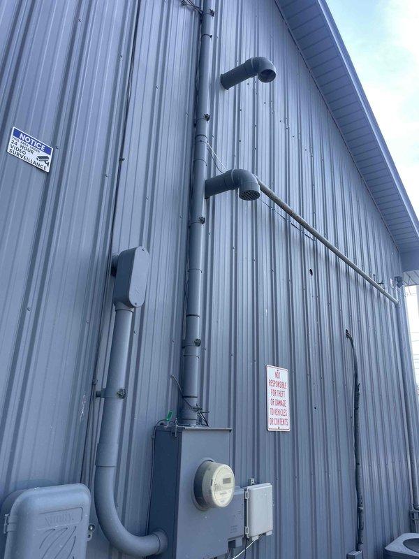 Completed commercial HVAC estimate for replacement of ceiling-mounted furnace unit that failed at end of previous winter season. Assessed existing hanging unit installation, documented exterior exhaust venting configuration with dual vertical stacks through metal siding, and evaluated electrical service connections including meter and disconnect panel. Photographed suspended air handler with support rod system, electrical panels, and PVC condensate drainage to provide comprehensive replacement specifications for customer approval.