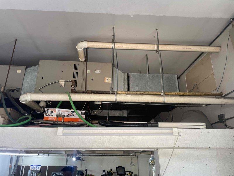 Completed commercial HVAC estimate for replacement of ceiling-mounted furnace unit that failed at end of previous winter season. Assessed existing hanging unit installation, documented exterior exhaust venting configuration with dual vertical stacks through metal siding, and evaluated electrical service connections including meter and disconnect panel. Photographed suspended air handler with support rod system, electrical panels, and PVC condensate drainage to provide comprehensive replacement specifications for customer approval.
