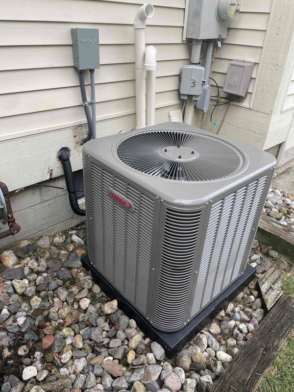 Completed installation of 2.5-ton Lennox air conditioning condenser unit with matching evaporator coil in left side yard location. Unit was positioned on rubber pad over wooden platform base in landscaped rock bed area, with all refrigerant lines, electrical conduit, and PVC drainage properly connected to existing residential electrical service and routed along exterior wall. System was successfully reconnected, tested, and verified operational per manufacturer specifications.