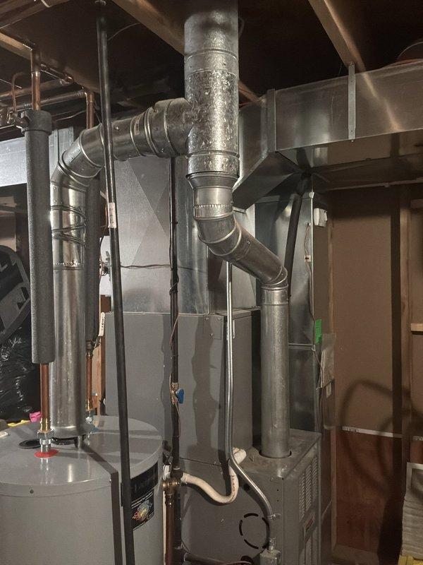 Conducted comprehensive evaluation of 22-year-old residential HVAC system for full replacement estimate. Assessed existing furnace installation in mechanical room, including extensive galvanized ductwork system, vertical cylindrical water heater integration, and copper piping configuration throughout basement utility space. Inspected exterior air conditioning condenser unit positioned on concrete pad, evaluating wire mesh protective housing, foundation ventilation components, and drainage systems. Documented all equipment specifications, ductwork layout, and mechanical connections through photographic records to provide accurate replacement system recommendations for aging equipment approaching end of service life.