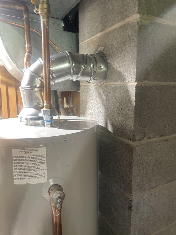 Completed water heater installation in residential basement utility room. Installed new white cylindrical water heater with proper copper piping connections and brass fittings at the top of the unit. Connected metallic vent pipe with elbow joint to redirect exhaust gases horizontally, ensuring proper ventilation and code compliance. All plumbing connections were secured with appropriate fittings and tested for leaks. Verified existing floor drain functionality in the installation area. Unit was properly positioned on concrete floor with adequate clearance for maintenance and safety requirements.