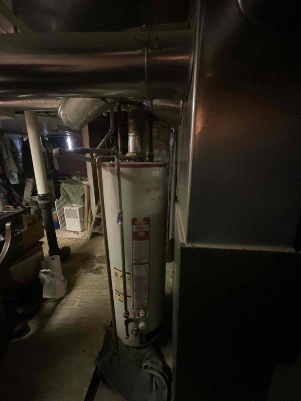 Conducted on-site assessment of aging gas water heater exhibiting significant rust deterioration at the base with active leaking. Documented existing unit specifications and installation configuration, including copper supply lines, gas connections, and venting system. Photographed water heater condition showing corrosion damage, moisture staining on concrete floor around unit base, and overall mechanical room layout with existing plumbing infrastructure. Evaluated replacement requirements and provided estimate for new gas water heater installation.