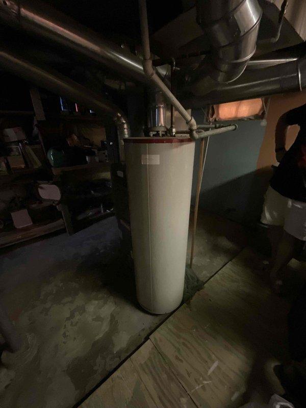 Conducted on-site assessment of aging gas water heater exhibiting significant rust deterioration at the base with active leaking. Documented existing unit specifications and installation configuration, including copper supply lines, gas connections, and venting system. Photographed water heater condition showing corrosion damage, moisture staining on concrete floor around unit base, and overall mechanical room layout with existing plumbing infrastructure. Evaluated replacement requirements and provided estimate for new gas water heater installation.
