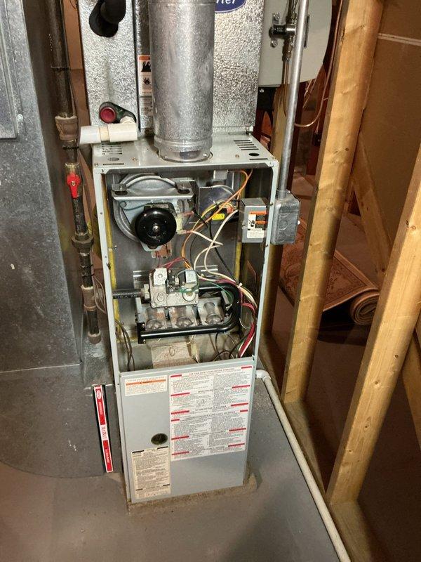 Responded to service call for 1997 A/C system in basement location reporting unusual humming noise and inadequate cooling performance. Upon inspection, accessed furnace cabinet to examine blower motor assembly, electrical connections, and control components. Evaluated thermostat operation and system controls, noting presence of older analog and digital programmable thermostats. Documented equipment condition through photography showing internal components including blower motor, gas valve assemblies, wiring, and control boards, as well as thermostat configuration displaying 76-degree reading at time of service.