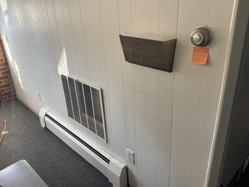 Provided estimate for complete HVAC system conversion from non-functional boiler heating to forced air furnace and air conditioning system. Existing outdoor condenser unit shows significant age and weathering with overgrown vegetation, while interior office space currently utilizes baseboard heating requiring full ductwork installation and equipment replacement for modernized climate control.