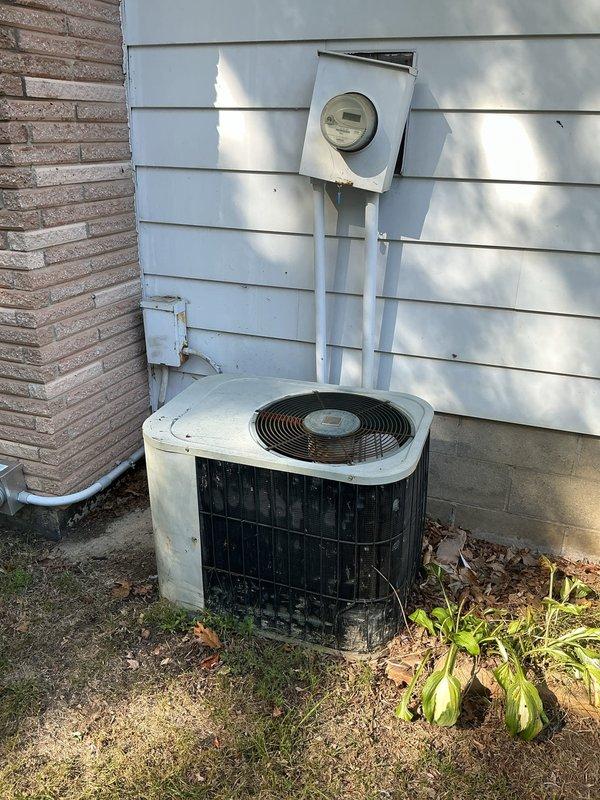 Responded to no cooling complaint on 15-year-old residential air conditioning system. Upon arrival, performed visual inspection of outdoor condensing unit and electrical connections. Documented existing equipment condition including outdoor unit placement, electrical meter configuration, and control panel wiring. System showed signs of age-related wear with weathering evident on unit exterior. Inspected electrical terminal connections, chassis grounding points, and wire routing within control panel. Photographed equipment for service records showing terminal block configuration numbered for circuit identification and multi-conductor wiring connections in various colors. Assessed outdoor unit positioning against building structure with adequate clearance for airflow. Noted standard residential installation with conduit routing from meter to equipment. Equipment accessible for service with no obstructions preventing maintenance access.