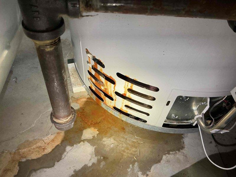 Responded to callback for hot water heater leak following previous day's HVAC installation. Inspected 110K BTU furnace and 3.5 ton A/C system with coil installation. Upon arrival, identified significant rust corrosion and water leakage at base of water heater unit, with moisture damage visible on concrete floor and ventilation grill showing extensive rust staining. Documented equipment condition with photos showing compromised water heater integrity and newly installed HVAC system components including flexible ductwork connections. Determined water heater failure unrelated to recent furnace and air conditioning installation work.