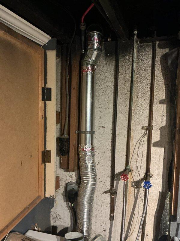 Responded to service call for dryer vent repair in residential property. Upon arrival, inspected the existing dryer exhaust vent system located in unfinished basement utility area. Found improperly installed flexible corrugated ductwork with multiple compromised sections and inadequate support brackets. Removed defective flexible corrugated section and replaced with code-compliant rigid metal duct sections, ensuring proper vertical run alignment. Installed new metal clamps and secure mounting brackets at all connection points to eliminate movement and potential disconnection. Verified proper venting pathway from dryer connection through basement ceiling structure. Documented installation with photographs showing before and existing conditions of basement mechanical space, including exposed framing, joists, and utility infrastructure. System tested and confirmed proper exhaust flow upon completion.