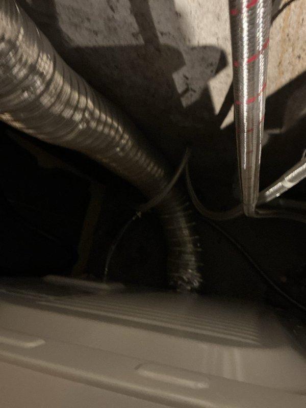Responded to service call for dryer vent repair in residential property. Upon arrival, inspected the existing dryer exhaust vent system located in unfinished basement utility area. Found improperly installed flexible corrugated ductwork with multiple compromised sections and inadequate support brackets. Removed defective flexible corrugated section and replaced with code-compliant rigid metal duct sections, ensuring proper vertical run alignment. Installed new metal clamps and secure mounting brackets at all connection points to eliminate movement and potential disconnection. Verified proper venting pathway from dryer connection through basement ceiling structure. Documented installation with photographs showing before and existing conditions of basement mechanical space, including exposed framing, joists, and utility infrastructure. System tested and confirmed proper exhaust flow upon completion.
