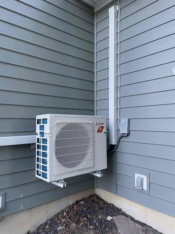 Completed full installation of Mitsubishi Electric mini-split heat pump system including outdoor condenser unit mounted on exterior wall with proper brackets, refrigerant line sets routed vertically with white line covers, electrical junction box installation, and new dedicated circuit. All mechanical and electrical permits obtained and work performed to code specifications, with system tested and operational upon completion.