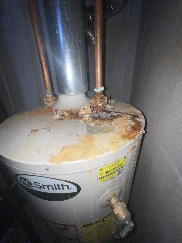 Conducted on-site assessment of gas water heater experiencing suspected leakage. Upon inspection, found extensive corrosion and rust accumulation at top pipe connections, including deteriorated copper and galvanized fittings with visible mineral deposits and water damage staining on tank surface. Water heater identified as A.O. Smith brand unit showing significant aging and lack of maintenance history, with no documented flushing performed during current occupancy period of approximately 9-10 years. Documented severe corrosion at hot and cold water inlet/outlet connections, compromised pipe threads, and rust-colored streaking indicating active or previous moisture intrusion. Photographed deteriorated conditions including corroded mounting brackets, mineral buildup around fittings, and overall tank degradation. Provided comprehensive replacement estimate for gas water heater installation due to advanced deterioration beyond economical repair.