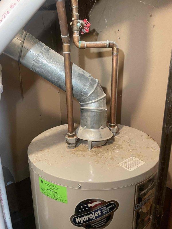 Responded to service call for malfunctioning water heater in confined utility closet space. Upon inspection, evaluated existing tanked water heater installation with inadequate clearance for proper service access and potential replacement. Unit showed signs of operational issues and was determined to be not functioning reliably. Documented current installation configuration including copper supply lines, galvanized vent piping, PVC drainage system, and shut-off valve locations. Assessed spatial constraints and determined that current clearances do not meet standard installation requirements for safe removal and replacement procedures. Provided estimate for standard tanked water heater replacement, noting that access limitations will require careful planning for equipment removal and new unit installation. Photographed existing conditions showing water heater positioning, plumbing connections, venting configuration, and available workspace dimensions for future reference during replacem
