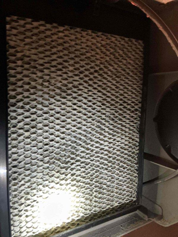 Completed annual HVAC maintenance inspection of air handling system and controls. Documented humidifier filter pad condition showing significant mineral scaling and deposits requiring replacement, and verified thermostat operation with system actively heating to maintain 75° setpoint with indoor conditions at 69° and 57% humidity.