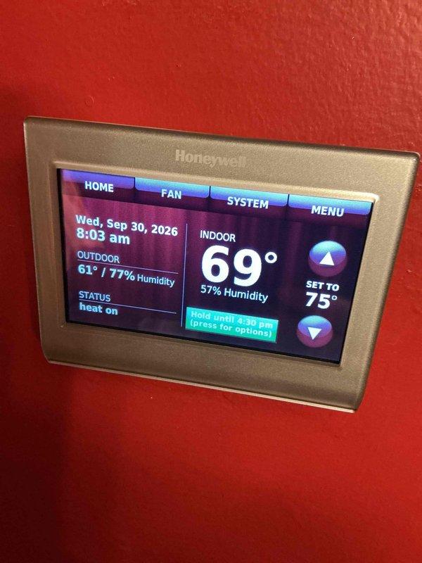 Completed annual HVAC maintenance inspection of air handling system and controls. Documented humidifier filter pad condition showing significant mineral scaling and deposits requiring replacement, and verified thermostat operation with system actively heating to maintain 75° setpoint with indoor conditions at 69° and 57% humidity.