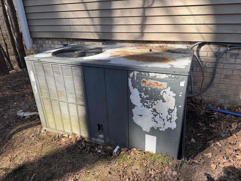 Conducted sales consultation for replacement of 20-year-old Goodman dual system. Visual inspection revealed severely deteriorated outdoor AC unit with extensive rust, corrosion, and weathering damage. Documented condition with photos showing the aged equipment and existing electrical setup including transfer switch and meter configuration for proper replacement planning.