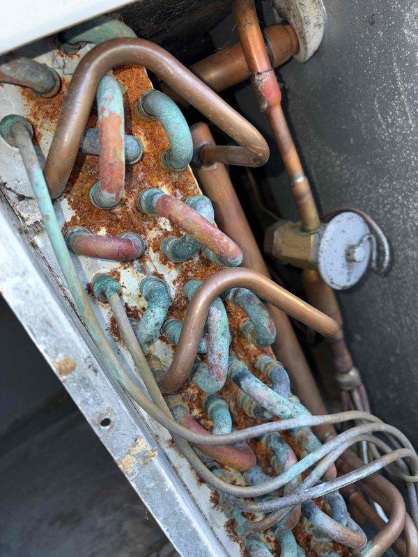 Responded to no heat service call. Upon inspection, found severe corrosion and oxidation on evaporator coil with significant blue-green patina formation on copper tubing. Determined that extensive deterioration of coils and accumulated debris in drain pan have compromised system functionality, requiring replacement of evaporator coil to restore heating operation.
