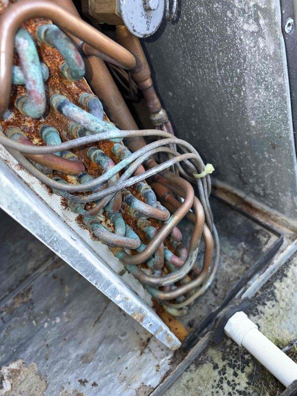 Responded to no heat service call. Upon inspection, found severe corrosion and oxidation on evaporator coil with significant blue-green patina formation on copper tubing. Determined that extensive deterioration of coils and accumulated debris in drain pan have compromised system functionality, requiring replacement of evaporator coil to restore heating operation.