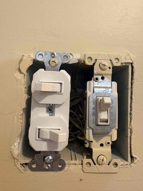 Responded to service call for non-functioning garage flood lights at a residential property built in 2002. Performed diagnostic troubleshooting to verify power supply to exterior lighting circuit. Inspected electrical wall box containing Cooper Circuit Guard toggle switch and duplex outlet, noting cosmetic wall damage around box perimeter. Traced circuit to main electrical panel and inspected breaker assembly, identifying proper breaker positions and verifying electrical connections. Confirmed power availability at circuit source and provided homeowner with assessment of lighting system functionality and available repair options for the non-operational flood light fixtures.