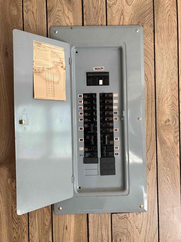 Responded to service call for newly drilled well requiring electrical power installation. Assessed existing residential electrical panel mounted on interior wood wall and evaluated routing requirements to run power from main distribution panel through crawlspace to blue pressure tank located adjacent to water storage tank. Documented panel configuration showing main breaker and dual columns of circuit breakers with current wire routing for future installation planning.