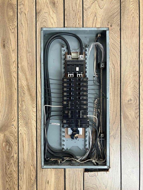 Responded to service call for newly drilled well requiring electrical power installation. Assessed existing residential electrical panel mounted on interior wood wall and evaluated routing requirements to run power from main distribution panel through crawlspace to blue pressure tank located adjacent to water storage tank. Documented panel configuration showing main breaker and dual columns of circuit breakers with current wire routing for future installation planning.