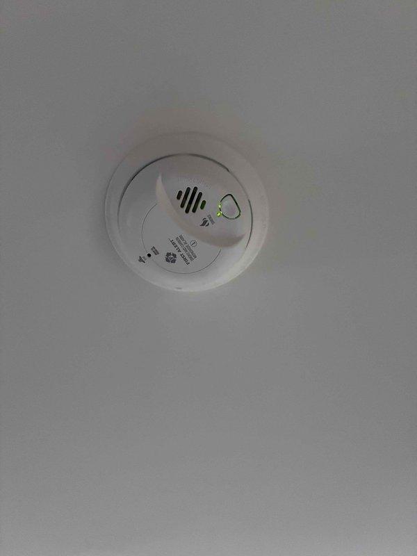 Responded to return visit for malfunctioning smoke detector that had been intermittently alarming since Thursday. Removed defective First Alert smoke detector from 12-foot ceiling and inspected hardwired electrical connections. Installed new smoke detector unit, secured wiring connections, tested device functionality, and verified proper operation of alarm system.