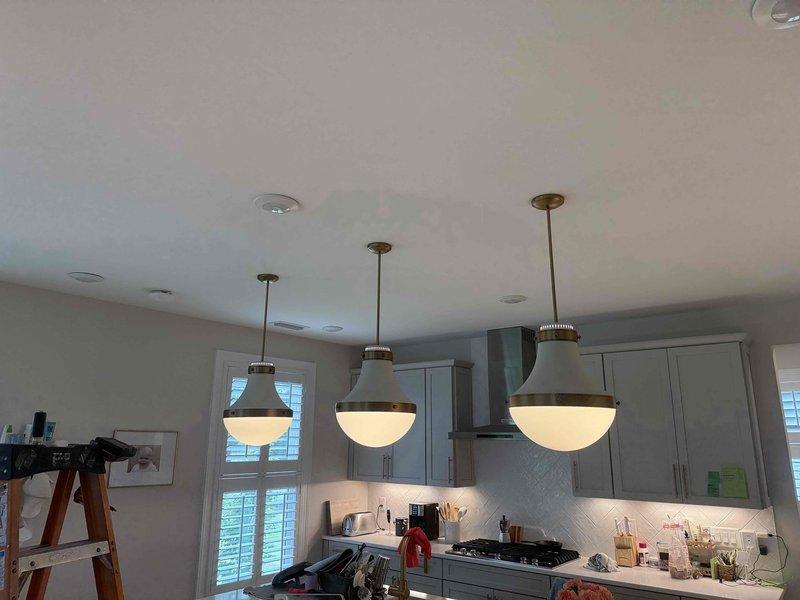 Successfully installed three homeowner-provided pendant light fixtures over the kitchen island, mounting each unit to the ceiling with proper electrical connections and ensuring secure attachment of the decorative glass shades. All fixtures were tested for proper operation, with switches functioning correctly and illumination confirmed across all three pendant lights.