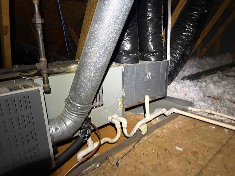 Responded to no cooling complaint on 24-year-old system. Upon arrival, confirmed unit was blowing air but not cooling. Inspected attic-mounted air handler and associated ductwork. Examined electrical connections, contactor assembly, and control components. Documented existing equipment configuration including silver metallic supply duct, black flexible return ductwork, condensate drainage system with PVC piping, and mounted control box. System showed age-appropriate wear on mechanical components including contactor housing with visible oxidation on brass elements and surface deterioration on painted surfaces. Photographed equipment for service records.