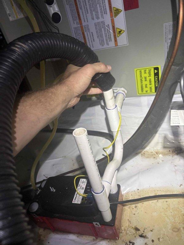 Responded to no-cool condition on downstairs unit of a two-system residence with 2021 equipment. Upon arrival, confirmed thermostat was set to 71°F but no airflow from registers and outdoor unit not energizing. Inspected air handler and found condensate pump failure causing safety float switch activation, which shut down system operation. Condensate drain pan showed significant sediment buildup and staining indicating prolonged water accumulation. Cleared blockage from condensate drain line, cleaned drain pan, and tested pump operation. Verified proper drainage flow through PVC condensate piping. Cycled system successfully with outdoor unit engaging and airflow restored to all registers. Upstairs unit operating normally with no issues noted.