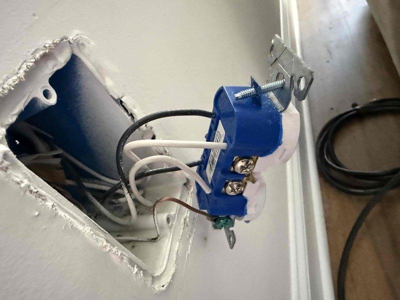 Completed comprehensive 32-point electrical system evaluation on 2020 residential property. Performed electrical panel maintenance including torque verification and connection inspection of all breaker terminals and bus bar connections. Conducted systematic testing of all GFCI outlets and breakers to verify proper ground fault protection and trip functionality. Tested all AFCI breakers to ensure arc fault detection circuits are operating within manufacturer specifications. Performed smoke and carbon monoxide detector maintenance including battery replacement and functional testing of all units. Replaced customer-supplied light bulbs in accessible fixtures up to 12 feet. Cleaned ceiling fans up to 12 feet in height. 

During inspection, identified exposed electrical junction box installation with incomplete wiring termination. Blue plastic outlet box mounted in wall cavity shows proper wire routing with black hot conductors, white neutral conductors, and bare copper ground wires present