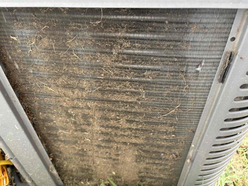 Responded to service call for downstairs system entering standby mode prematurely and inadequate cooling, with indoor temperature reaching 80 degrees after only 5 hours of runtime. Upon inspection of the 10-year-old outdoor condenser unit, found extensive accumulation of dirt, grass clippings, organic debris, and matted fibrous material heavily restricting airflow through the condenser coils and heat exchanger fins. The buildup was significantly impacting system efficiency and causing the unit to overheat and shut down prematurely. Documented the condition of the dirty coils with photographs showing the severity of contamination on both exterior surfaces and between the aluminum fins, which would require thorough cleaning to restore proper system operation and prevent continued thermal shutdowns.