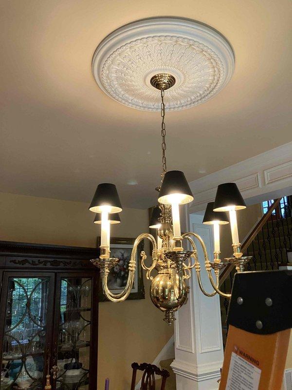 Installed a five-arm brass chandelier with decorative candle-style fixtures and black lampshades in the kitchen dining area, mounting it to an ornate ceiling medallion at standard ceiling height. Completed electrical wiring connections and installed a three-switch toggle assembly in the wall to control the lighting fixture. Verified proper operation of all switches and confirmed the chandelier is functioning correctly with secure mounting and safe electrical connections.