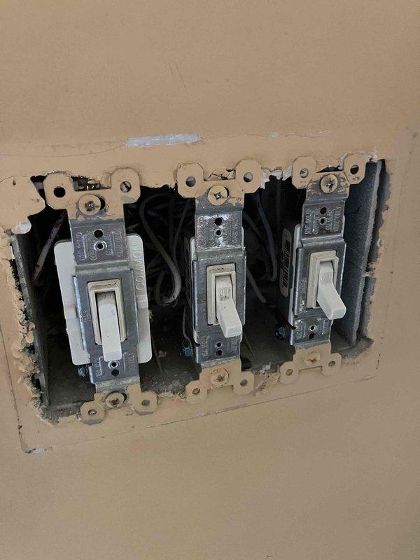 Installed a five-arm brass chandelier with decorative candle-style fixtures and black lampshades in the kitchen dining area, mounting it to an ornate ceiling medallion at standard ceiling height. Completed electrical wiring connections and installed a three-switch toggle assembly in the wall to control the lighting fixture. Verified proper operation of all switches and confirmed the chandelier is functioning correctly with secure mounting and safe electrical connections.
