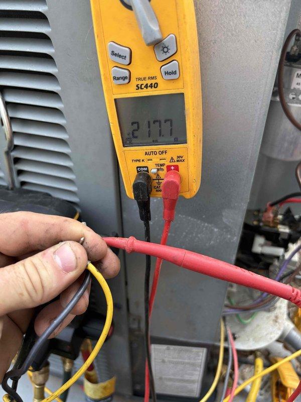 Responded to no cooling complaint on 4-year-old system where indoor blower was operational but outdoor condenser fan was not running. Performed diagnostic testing at air handler and outdoor unit using electrical meter to verify power supply and component operation. Measured voltage readings at outdoor unit showing 21.77 volts, indicating potential capacitor failure or compressor/fan motor electrical issue preventing proper condenser fan operation, resulting in loss of cooling capacity.