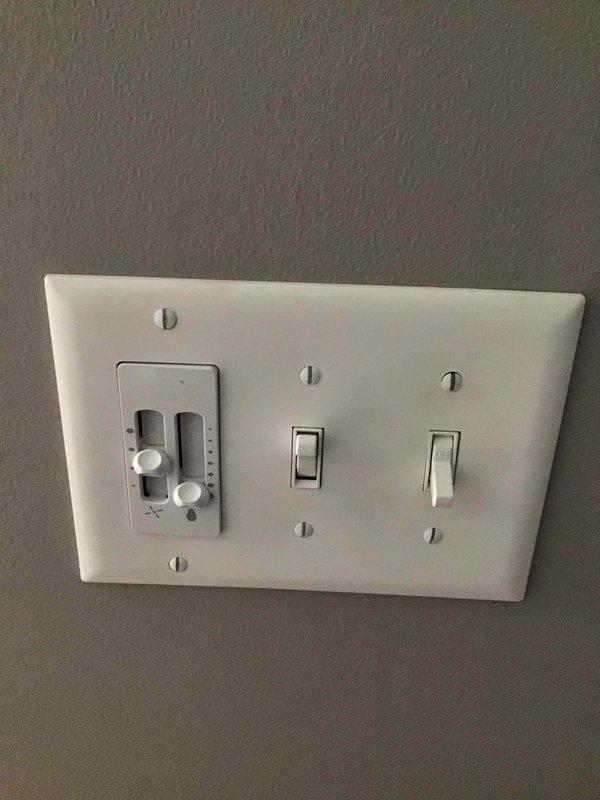 Installed customer-provided in-wall fan control switches and standard toggle switches in a triple-gang configuration on interior wall. Mounted combination switch plate covers to complete the installation, providing operational control for ceiling-mounted fan unit with integrated lighting fixture.