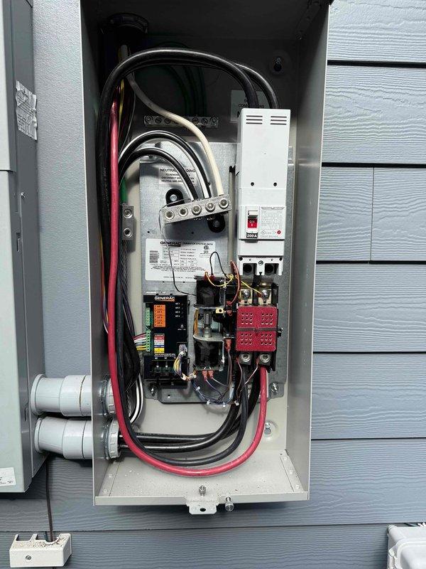 # Electrical Panel Surge Protector Service

Responded to service call for exterior surge protector displaying red indicator light and audible alarm. Inspected main electrical panel and associated equipment including meter base, Generac transfer switch, and whole-house surge protection device. Found surge protector had reached end of service life as indicated by red LED status indicator and alarm condition. The white rectangular surge protective device mounted in the main panel showed compromised MOV (metal oxide varistor) components, requiring replacement to restore proper surge protection to the electrical system. Verified all electrical connections, panel components, and grounding system were secure and functioning properly. Generator transfer switch and associated equipment operating normally with no issues detected.