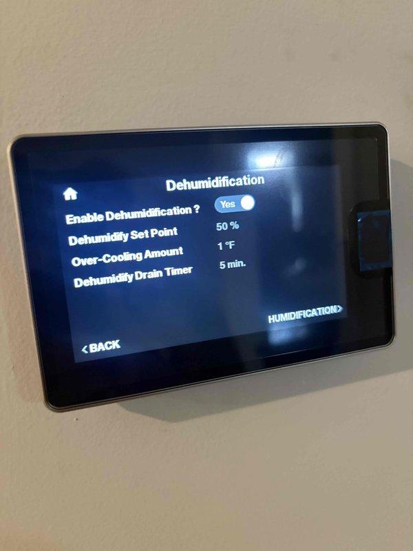 Completed installation and configuration of zoning system with advanced climate control capabilities. Programmed wall-mounted smart thermostat with dehumidification settings, establishing 50% humidity set point with 1°F over-cooling amount and 5-minute dehumidification drain timer. Verified proper system operation with cooling function active and humidity monitoring displaying 71% current reading at 72°F ambient temperature.