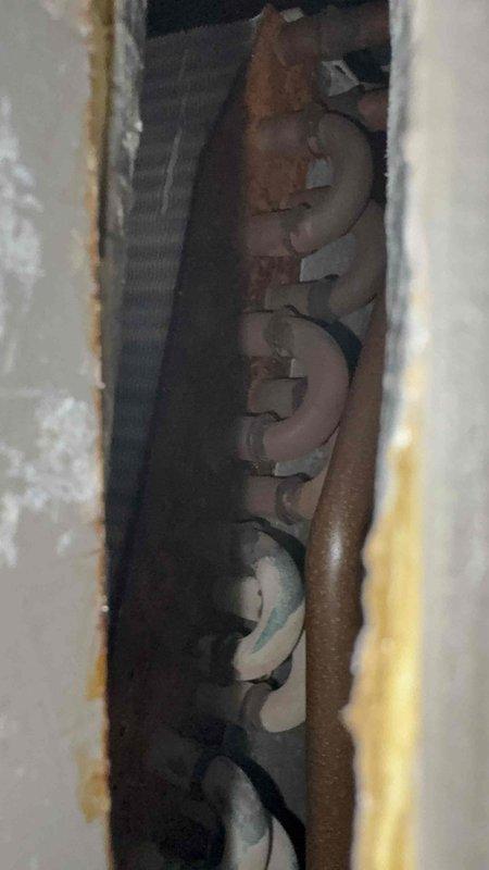 Responded to service call for upstairs HVAC system not operating properly in a two-system residence with equipment 10-20 years old. Homeowner reported repeated breaker trips affecting both bedroom lighting circuit and AC unit, with upstairs system blowing ambient temperature air and air handler fan failing to operate. Upon arrival, investigated electrical issues and inspected attic-mounted HVAC equipment, ductwork, and associated electrical connections. Examined wall cavity access point showing copper refrigerant lines and related infrastructure. Assessed galvanized metal supply duct, flexible return ductwork, and air handler installation in attic space. Documented breaker condition and evaluated electrical supply to upstairs HVAC unit to determine cause of intermittent tripping and system failure.