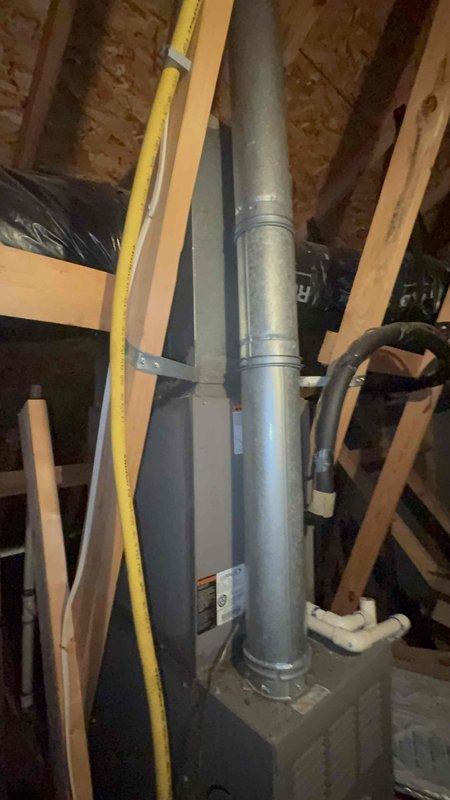 Responded to service call for upstairs HVAC system not operating properly in a two-system residence with equipment 10-20 years old. Homeowner reported repeated breaker trips affecting both bedroom lighting circuit and AC unit, with upstairs system blowing ambient temperature air and air handler fan failing to operate. Upon arrival, investigated electrical issues and inspected attic-mounted HVAC equipment, ductwork, and associated electrical connections. Examined wall cavity access point showing copper refrigerant lines and related infrastructure. Assessed galvanized metal supply duct, flexible return ductwork, and air handler installation in attic space. Documented breaker condition and evaluated electrical supply to upstairs HVAC unit to determine cause of intermittent tripping and system failure.