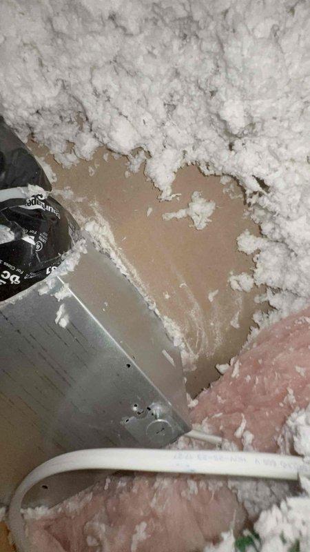 Responded to complaint of recurring mildew stains around master bathroom exhaust fan. Inspected attic space above bathroom and found improper exhaust fan termination with inadequate venting causing moisture accumulation in ceiling cavity. Documented damaged insulation and drywall deterioration around exhaust ductwork, along with improperly secured electrical junction box and wiring connections that required attention for code compliance and safety.