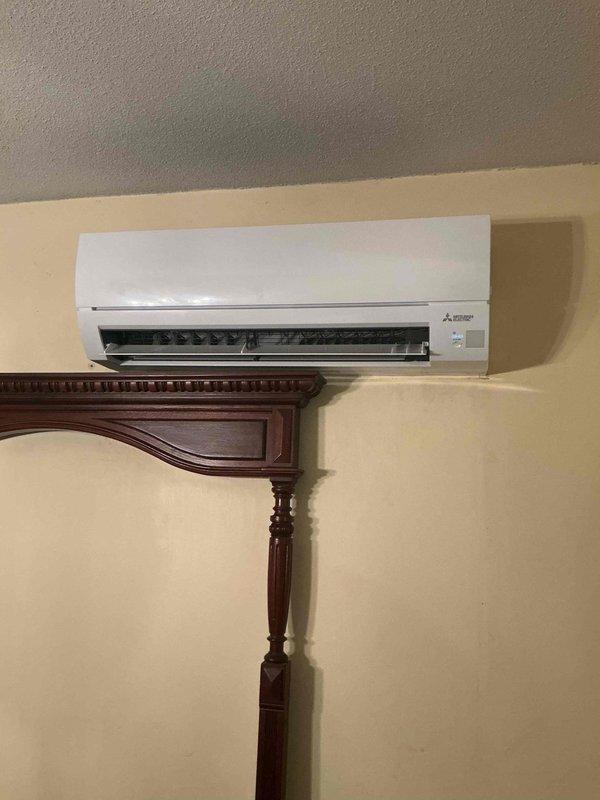 Completed installation of Mitsubishi Electric ductless mini-split air conditioning system. Mounted indoor wall unit on interior cream-colored wall and installed outdoor condenser unit. Ran refrigerant lines and electrical connections through wall penetration, secured condensate drain line, and verified proper system operation with successful startup and testing.