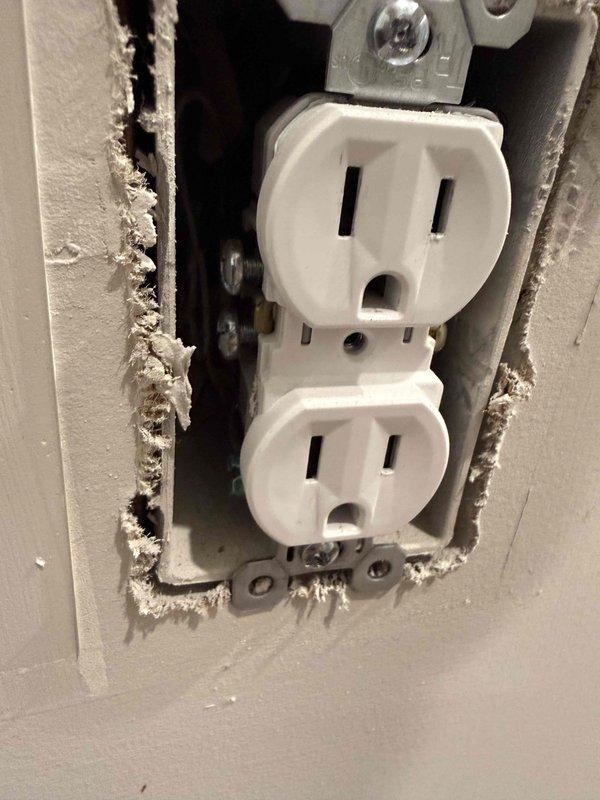 Completed annual 32-point electrical system evaluation on 2019 residential property. Performed electrical panel maintenance including torque verification and connection inspection of all terminations. Tested all GFCI outlets and breakers for proper shock protection functionality and confirmed arc fault breakers were operating within specifications for fire protection. Conducted smoke and carbon monoxide detector maintenance including battery replacement and operational testing of all units. Inspected exterior disconnect box and verified proper wire terminations on terminal block with black, red, and green conductors properly secured. Identified damaged drywall surrounding interior outlet requiring repair, with outlet itself functioning properly despite compromised wall material around electrical box opening. Replaced customer-supplied light bulbs in fixtures up to 12 feet and performed ceiling fan cleaning service. All electrical components tested and verified operational per manufactu