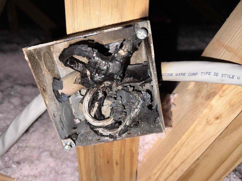 Responded to report of insufficient power to AC disconnect box as identified by HVAC technician. Upon investigation, discovered severely fire-damaged electrical junction box with completely charred wiring and melted insulation indicating previous electrical fire or extreme heat event. Measured voltage at 228V AC using Fluke T5-1000 electrical tester. Junction box mounted to wooden framing showed extensive internal carbonization and heat distortion of metal components, rendering the electrical connection unsafe and non-functional. Documented hazardous condition and recommended immediate replacement of damaged junction box, all affected wiring, and thorough inspection of circuit to ensure safe restoration of proper power supply to AC disconnect.