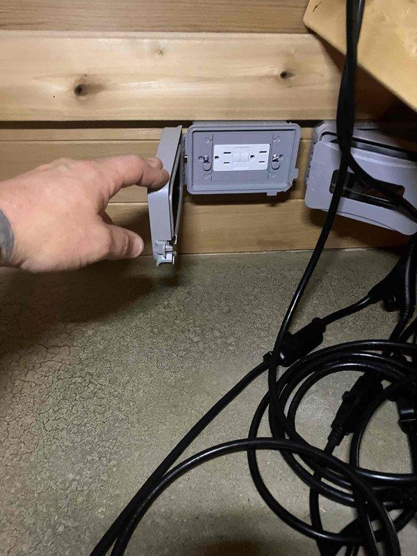 Installed a new weatherproof electrical outlet in the sauna by tapping into the existing lighting circuit. Ran Romex cable through the attic space, secured wiring at junction box, and mounted a gray flip-up style outlet cover on the wooden wall. Customer was advised that adding this outlet to the lighting circuit may cause the breaker to trip under heavy load conditions.