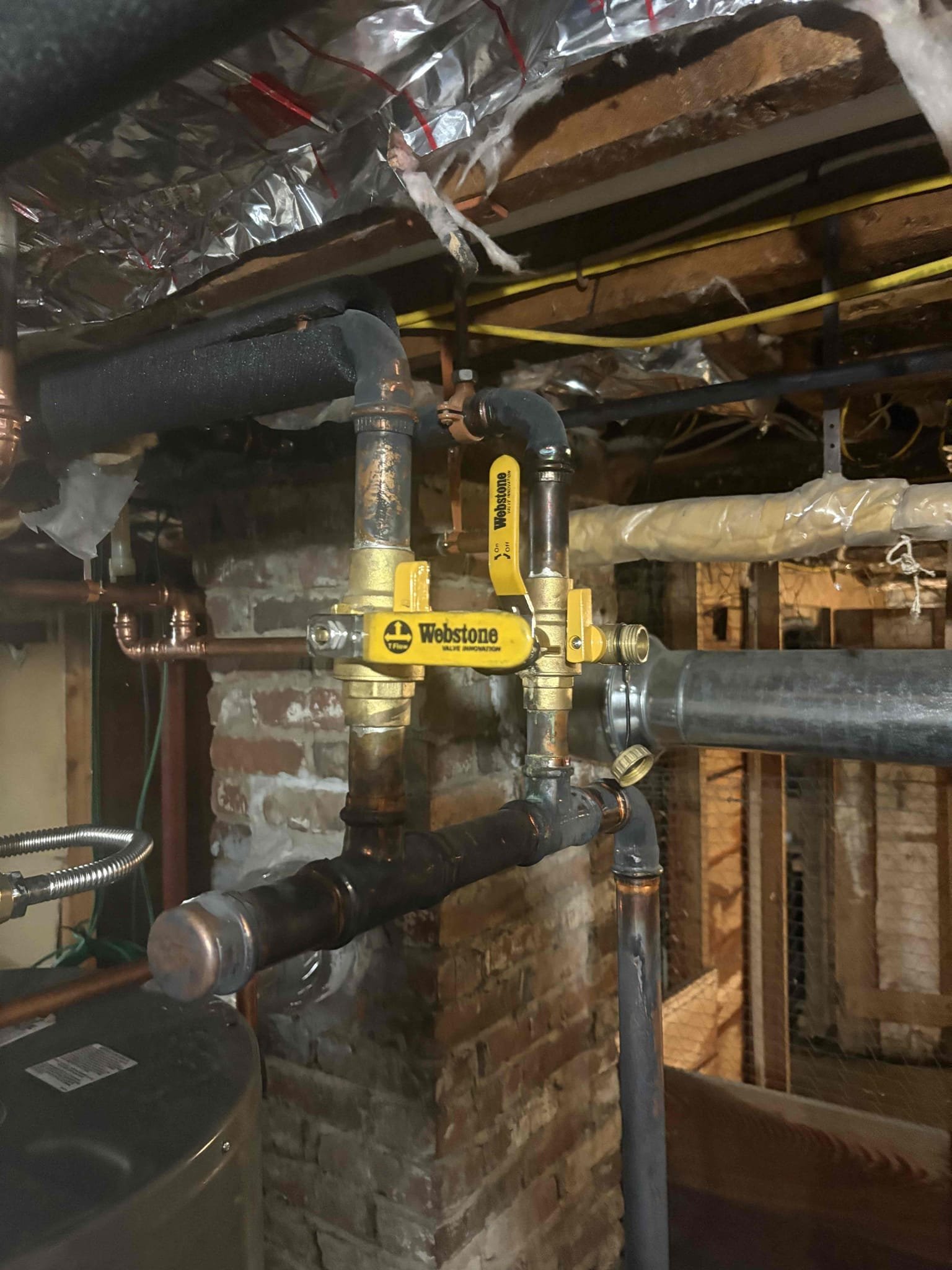 Responded to a report of a leak in the living room and found significant water and black debris around the baseboard. Inspection revealed a hole in the baseboard piping, likely caused by freezing. I isolated the first-floor heating zone and confirmed that the upstairs zone was leak-free and circulating properly, with the upstairs thermostat set to 70 degrees and the first-floor thermostat off. I restored water to the house and verified that no additional leaks were present. Both downstairs mini-split units were turned on and set to 75 degrees in heat mode to maintain temperature. During testing, I found that the first-floor thermostat was intermittently opening and closing the call for heat, indicating a malfunction that may have prevented the zone from heating correctly. We will return shortly to evaluate the necessary repairs.