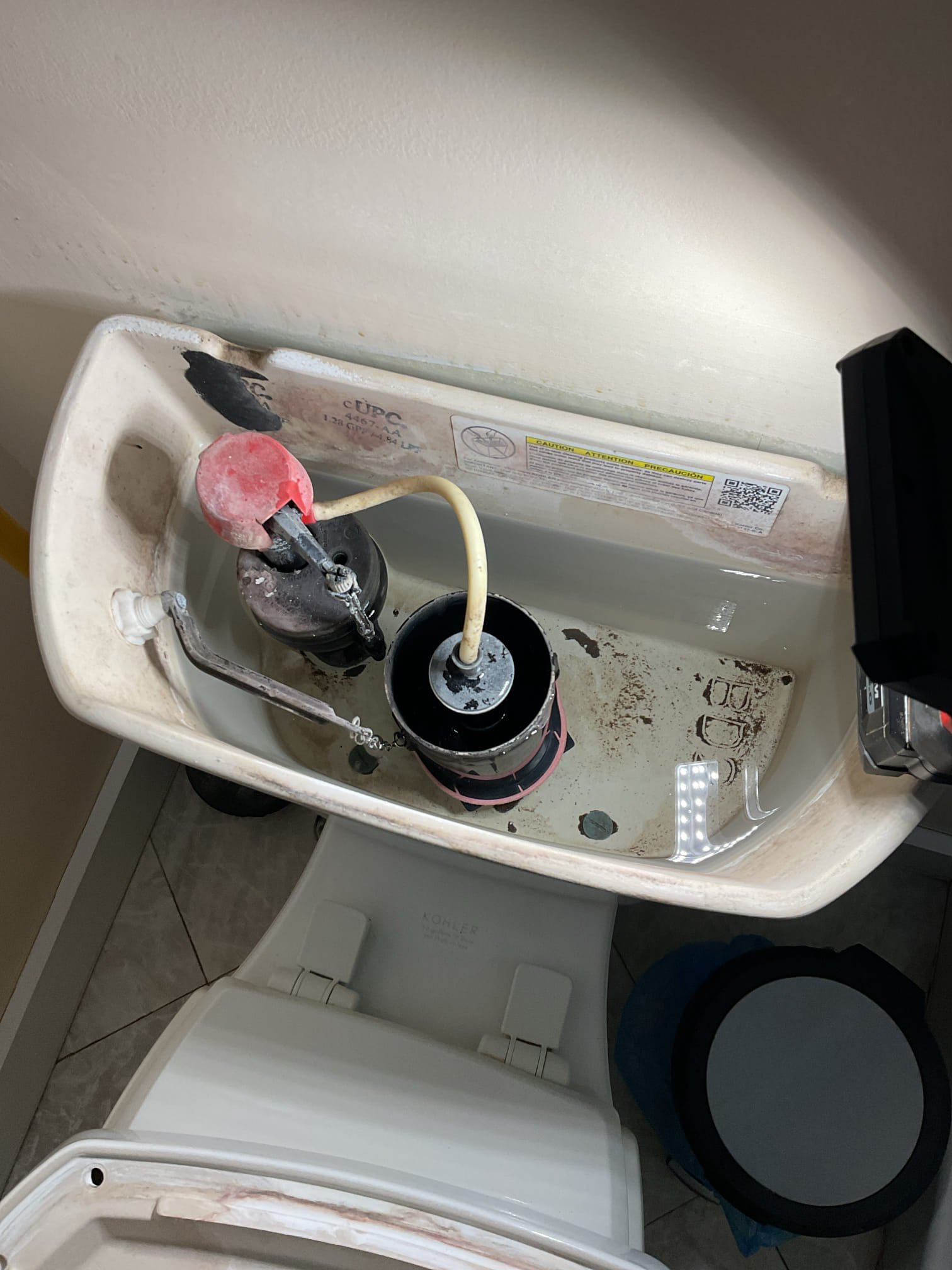 The Kohler toilet was experiencing inconsistent flushing due to worn internal components caused by hard water buildup. Upon inspection, the flush seal was found to be deteriorated and no longer providing a proper watertight seal, and the fill valve was malfunctioning due to calcium buildup, contributing to constant running water. The water supply to the toilet was shut off and the tank was drained, after which the flush seal, fill valve, and supply line were replaced. The system was restored and tested, confirming proper operation with no leaks present; a dye test was performed and verified a complete seal with no water transfer to the bowl after 20 minutes.