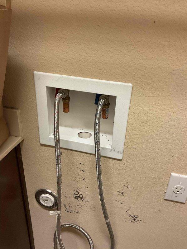 Responded to service call for leaking washing machine supply valves in a 12-year-old home. Diagnosed water damage beneath recessed laundry box with visible staining on wall. Replaced faulty washing machine valves and supply lines, restoring proper function and preventing further water damage.