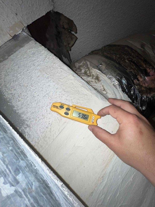 Performed spring maintenance on a 24-year-old HVAC system located in the attic of a 43-year-old home. Found significant debris accumulation (leaves, twigs, dirt) inside the unit which was cleaned out to improve system efficiency. Temperature readings with digital meter showed 53.6°F at the ductwork, and noted damaged insulation requiring attention in the attic space.