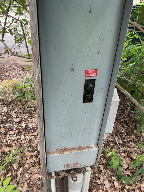Responded to service call for newly installed water heater with no power supply in 1969 residential property. Inspected outdoor service disconnect panel mounted on utility pole and main electrical panel located in enclosed crawlspace area beneath home. Verified existing panel configuration and circuit availability for electric water heater connection. Documented weathered outdoor disconnect showing age-related deterioration and moisture staining at base. Photographed new PRO+40 M2 RHOS electric water heater unit with visible manufacturer specifications indicating 240V electrical requirements. Assessed electrical distribution system capacity and confirmed no amperage delivery to water heater circuit as reported, preventing operation of new appliance installation.