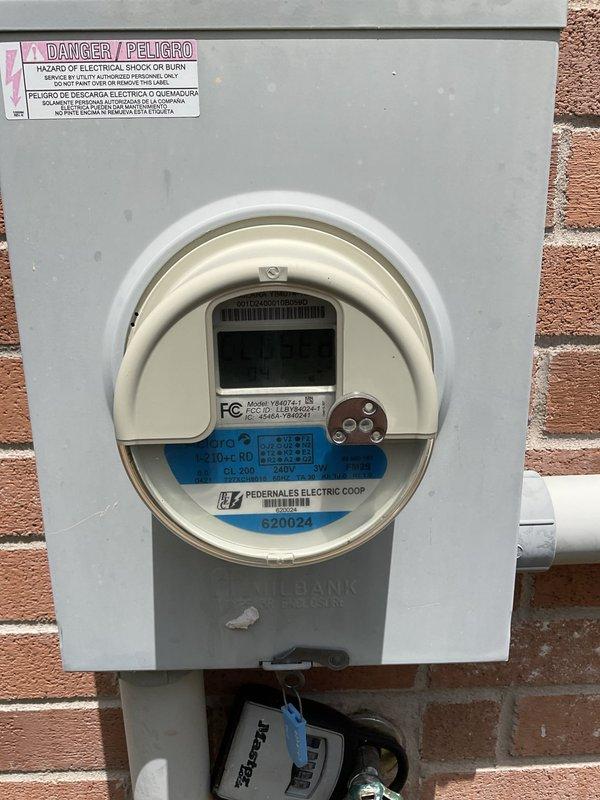 Responded to service call for breaker tripping issue affecting office circuit in 2013 home with electrical panel located in garage. Inspected main electrical panel and meter assembly, documenting current panel configuration with multiple circuits and wiring connections. Photographed exterior meter installation showing Pedernales Electric Coop digital meter mounted on brick exterior with proper conduit and grounding, as well as interior panel box with dual columns of circuit breakers and color-coded wiring distribution. Evaluated breaker functionality and circuit loading conditions to identify source of repeated tripping on office circuit.